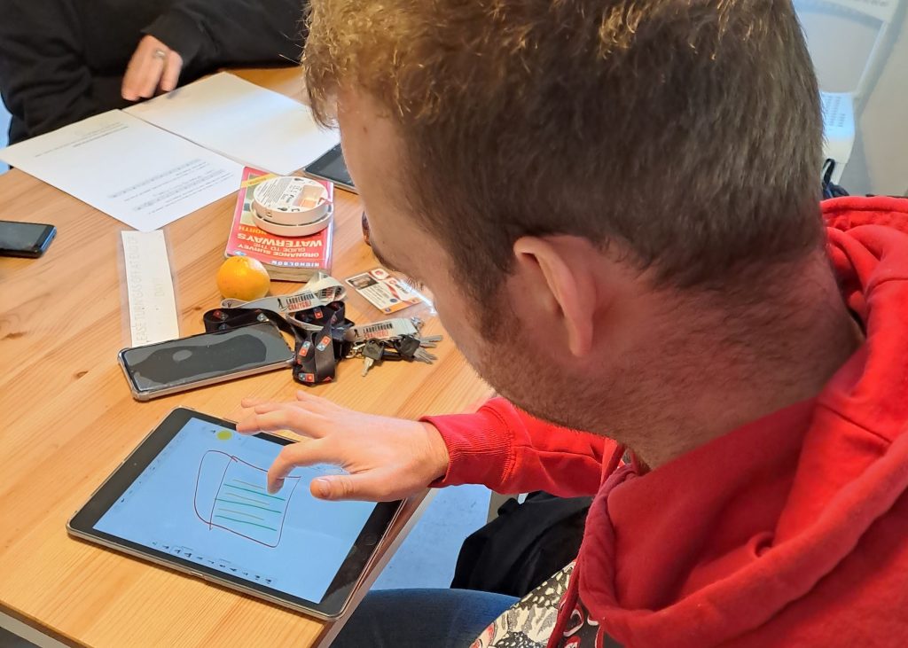 A service user is sat at a desk and using an iPad as a drawing tablet.